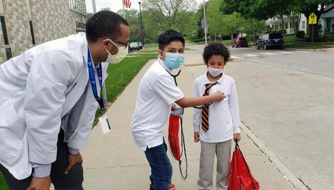 child listening to another child's pulse with a stethoscope while an adult watches