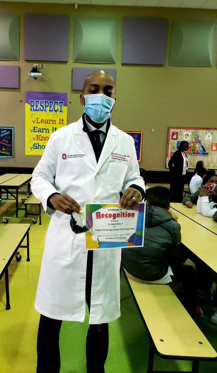 adult in labcoat holding a recognition certificate