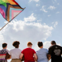 group of people locking arms while a PRIDE flag flies over