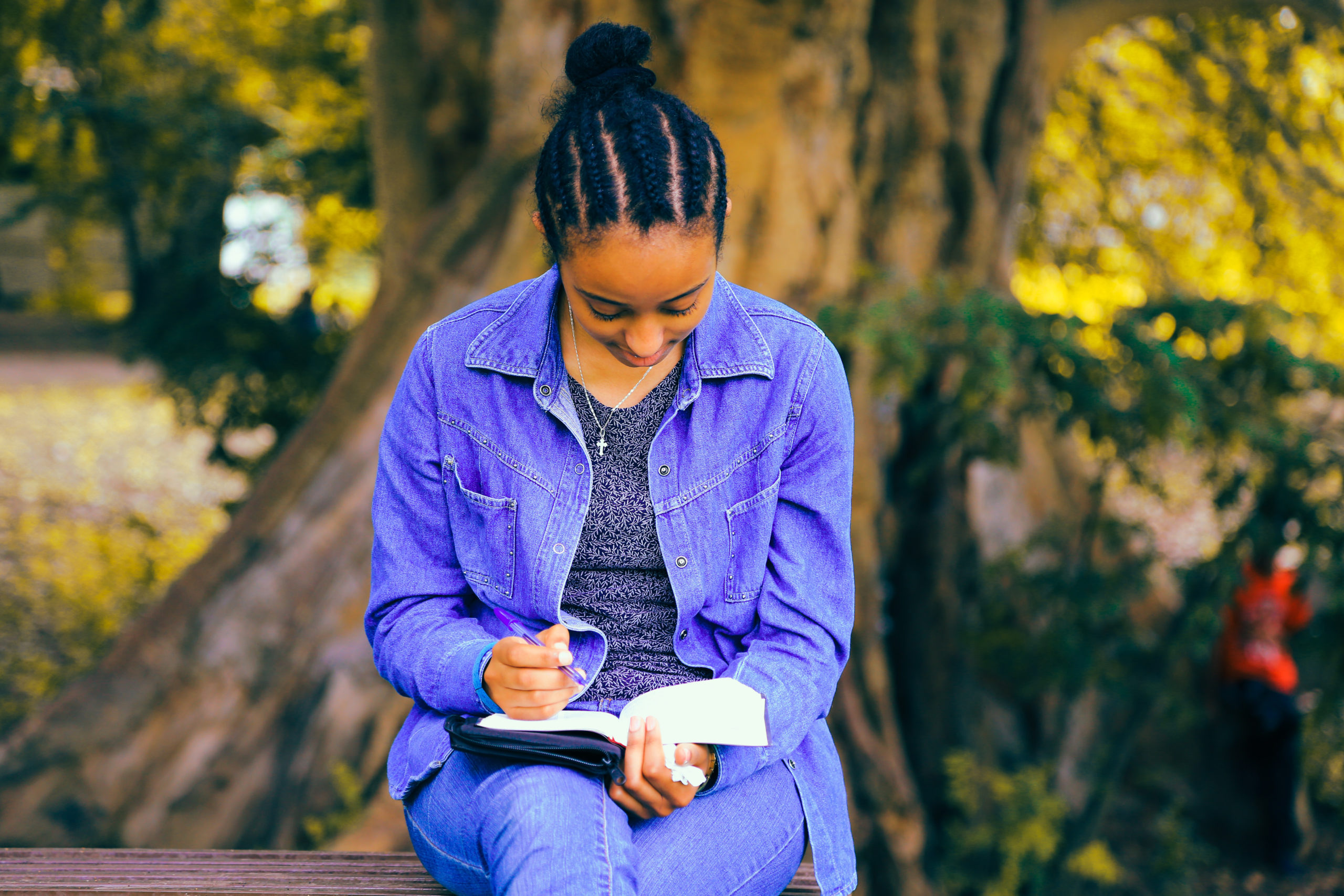 photo of a young Black girl reading in front of a tree