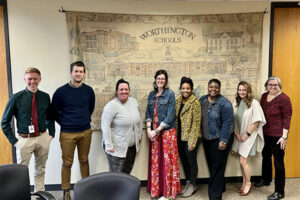 group of teachers and administrators in front of a tapestry that says Worthington Schools