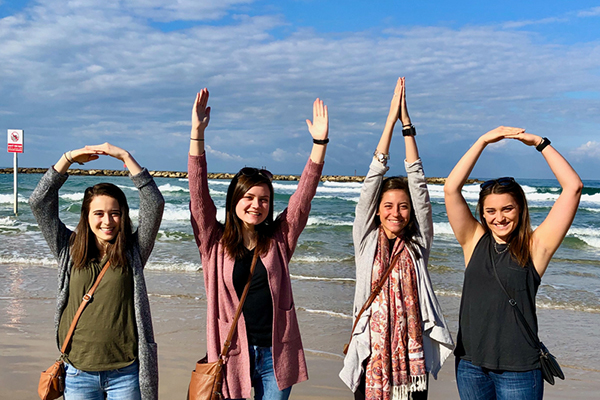 A group of people spelling out OHIO with their arms in front of a beach