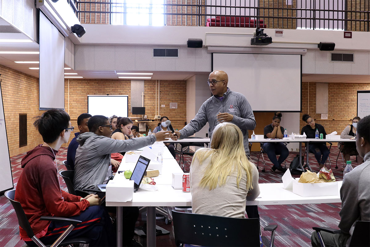 Photo of Don Pope-Davis giving a microphone to a student sitting at a table