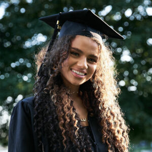 A woman looking at the camera smiling with a graduation cap and gown on