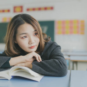A teenage girl in a classroom holding a book looking away from the camera