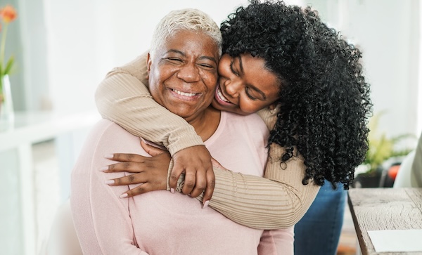 a caregiver gives their elder person a hug, both are smiling