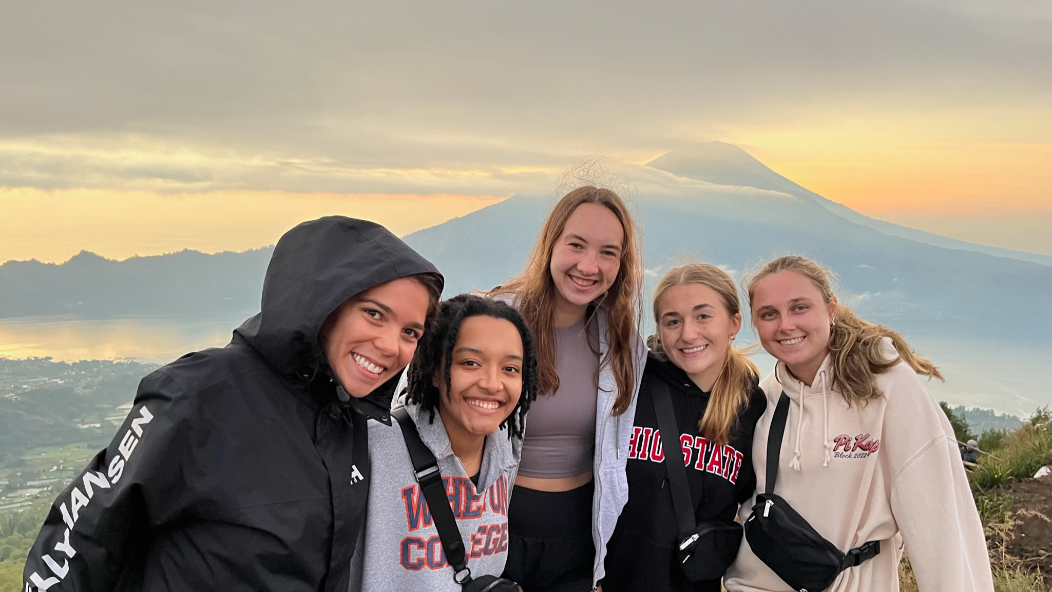 A group of students standing in front of a sunset with a mountain in the background.