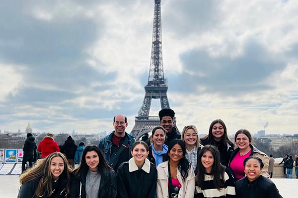 A group of smiling students standing in front of the Eiffel Tower
