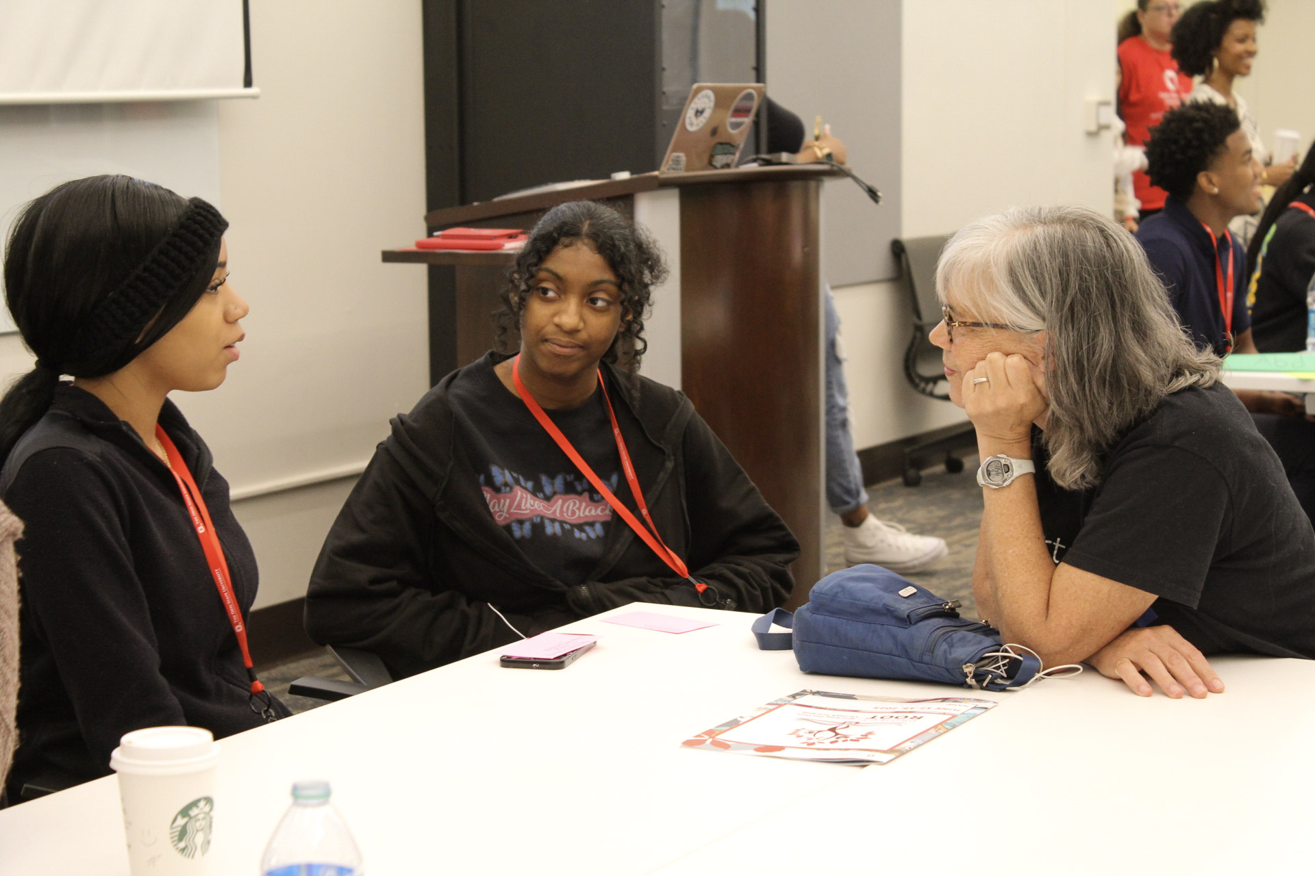 An EHE Faculty member leans in to listen to two students sitting at a table.