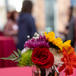 Flower centerpiece is the focus of this picture with a blurry silhouette of people in the background.