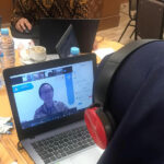 A person with headphones sits and watches Ivan Stefano, PhD on the zoom call on their laptop.