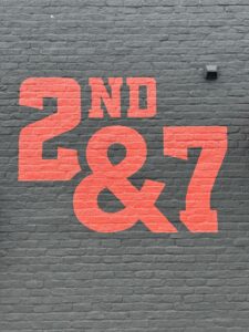 2nd & 7 logo painted on a black brick wall