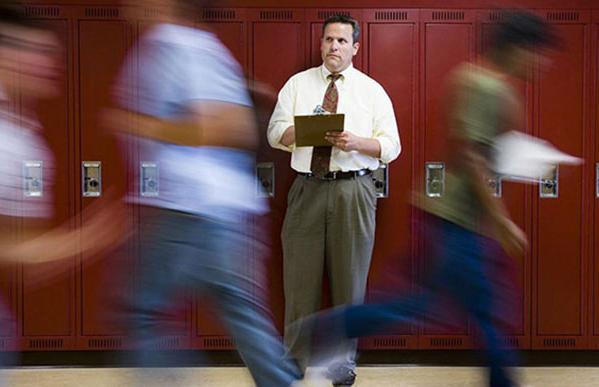 teacher stand in front of locker with students walking pass